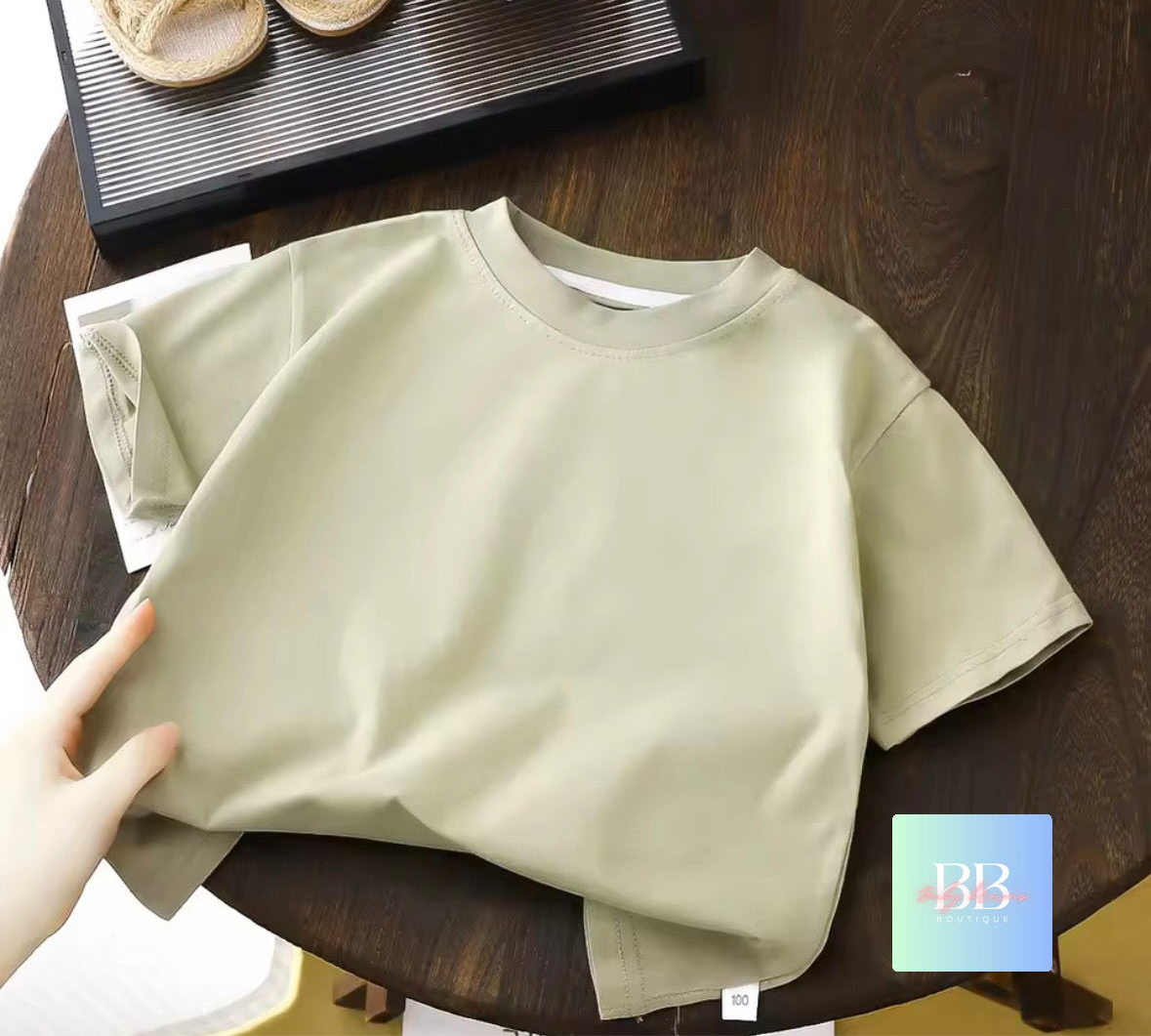 Beige t-shirt on a wooden table with a hand holding it