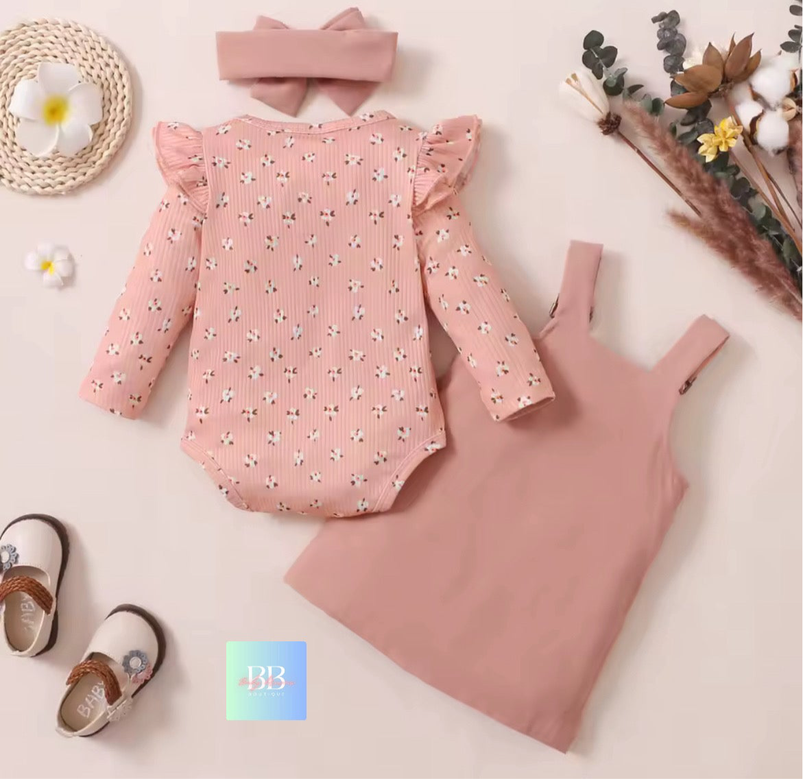 Pink baby outfit with romper, dress, and shoes on a light background