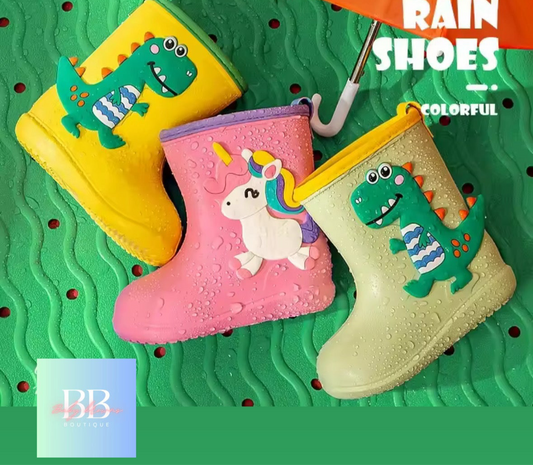 Three colorful rain boots with dinosaur and unicorn designs on a green textured background.