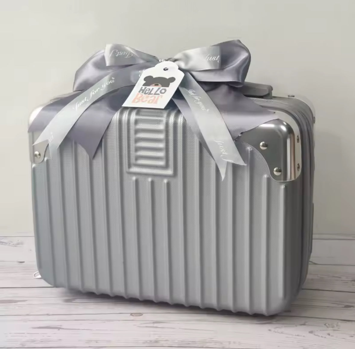 Silver suitcase with a gray ribbon and tag on a light wooden floor.