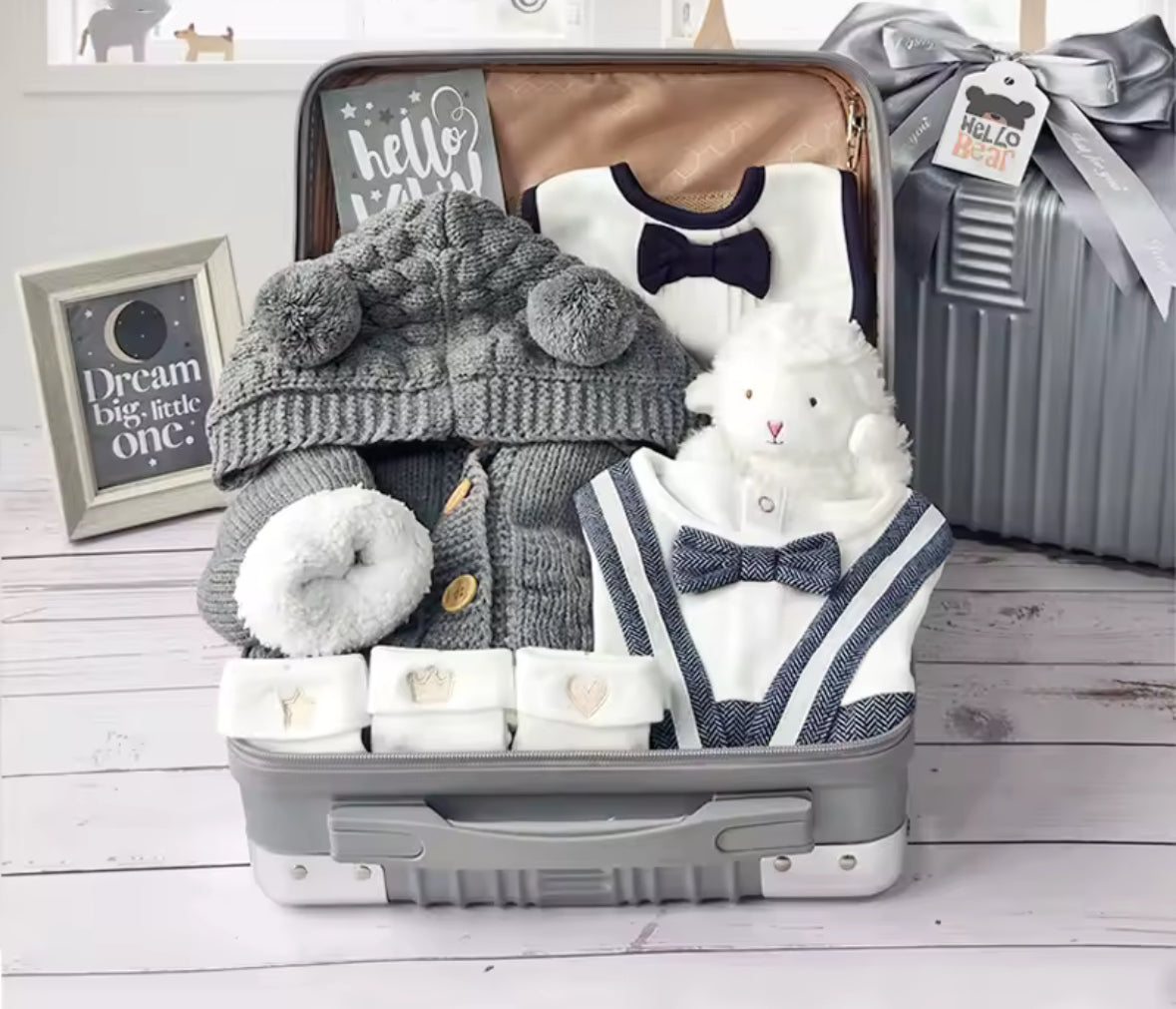 Baby gift set in a suitcase with a gray hat, white bear, and baby clothes on a wooden floor.