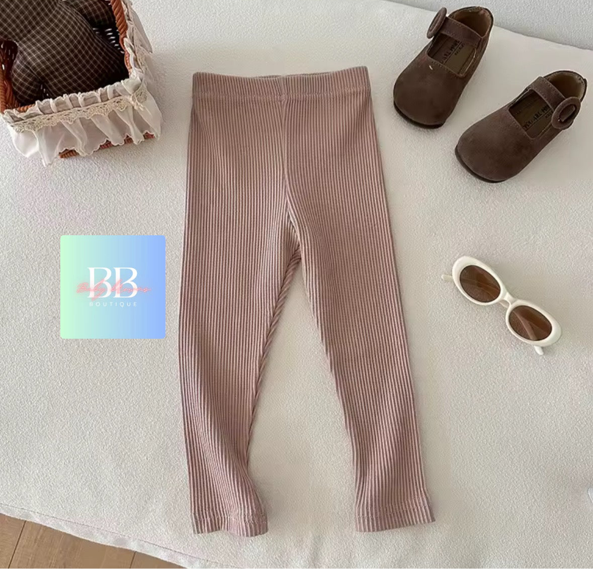 Brown ribbed leggings with baby shoes and sunglasses on a white surface, featuring the brand 'BB'.