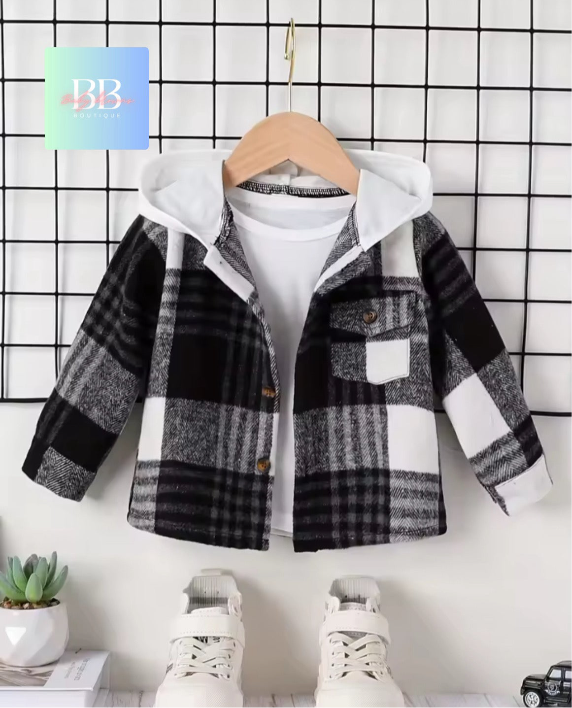 Plaid jacket with white hoodie on a hanger against a grid-patterned wall.