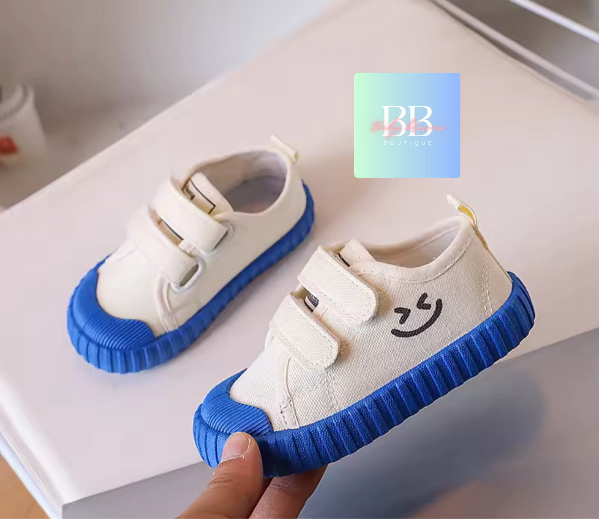 White children's shoes with blue soles held by a hand on a light background