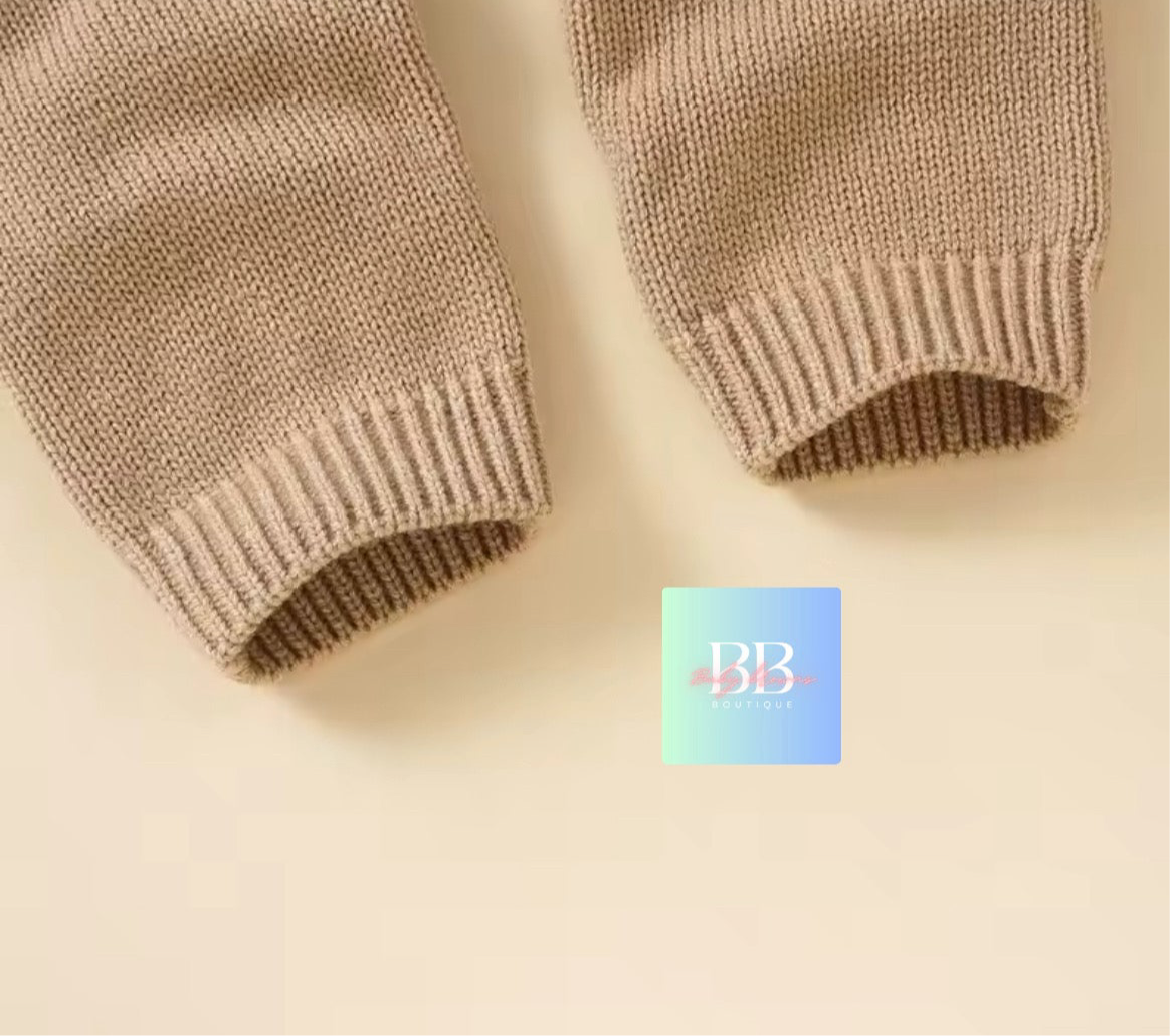 Close-up of beige knitted sleeves on a beige background with a brand logo in the corner.