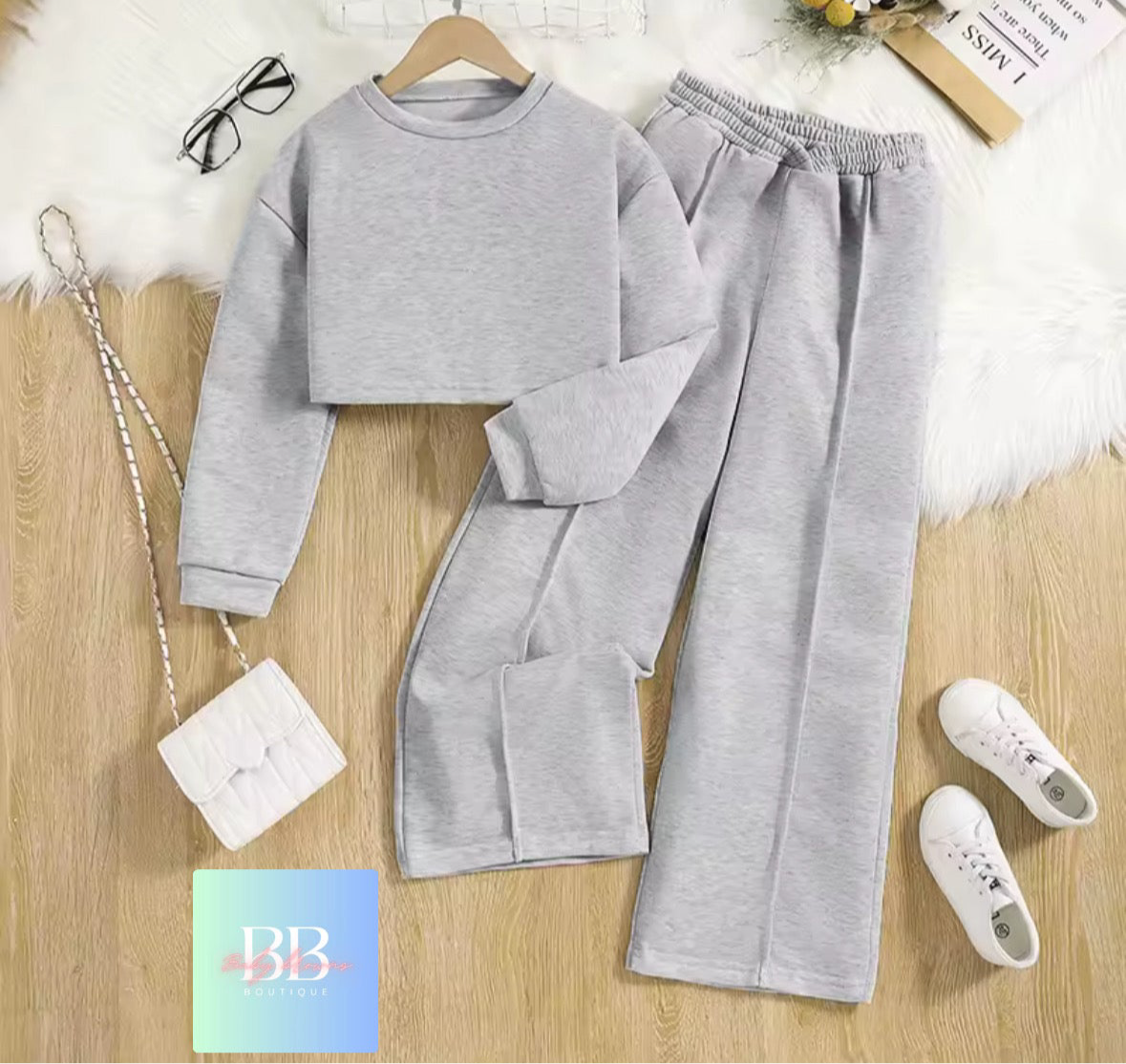 Gray sweatshirt and pants set on a wooden floor with a white bag and sneakers.