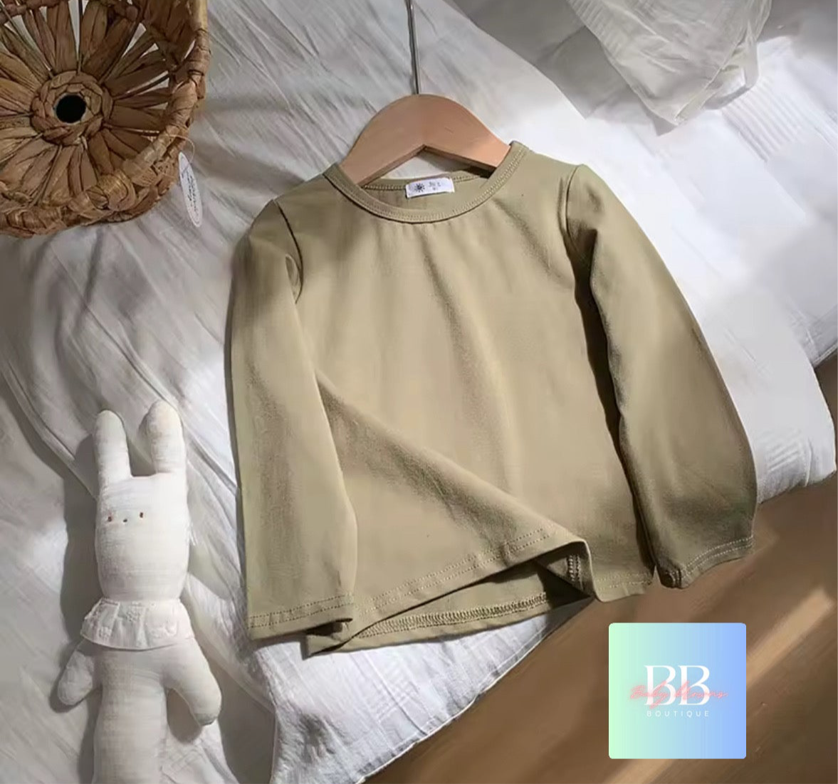 Beige sweatshirt on a hanger with a white plush toy on a bed