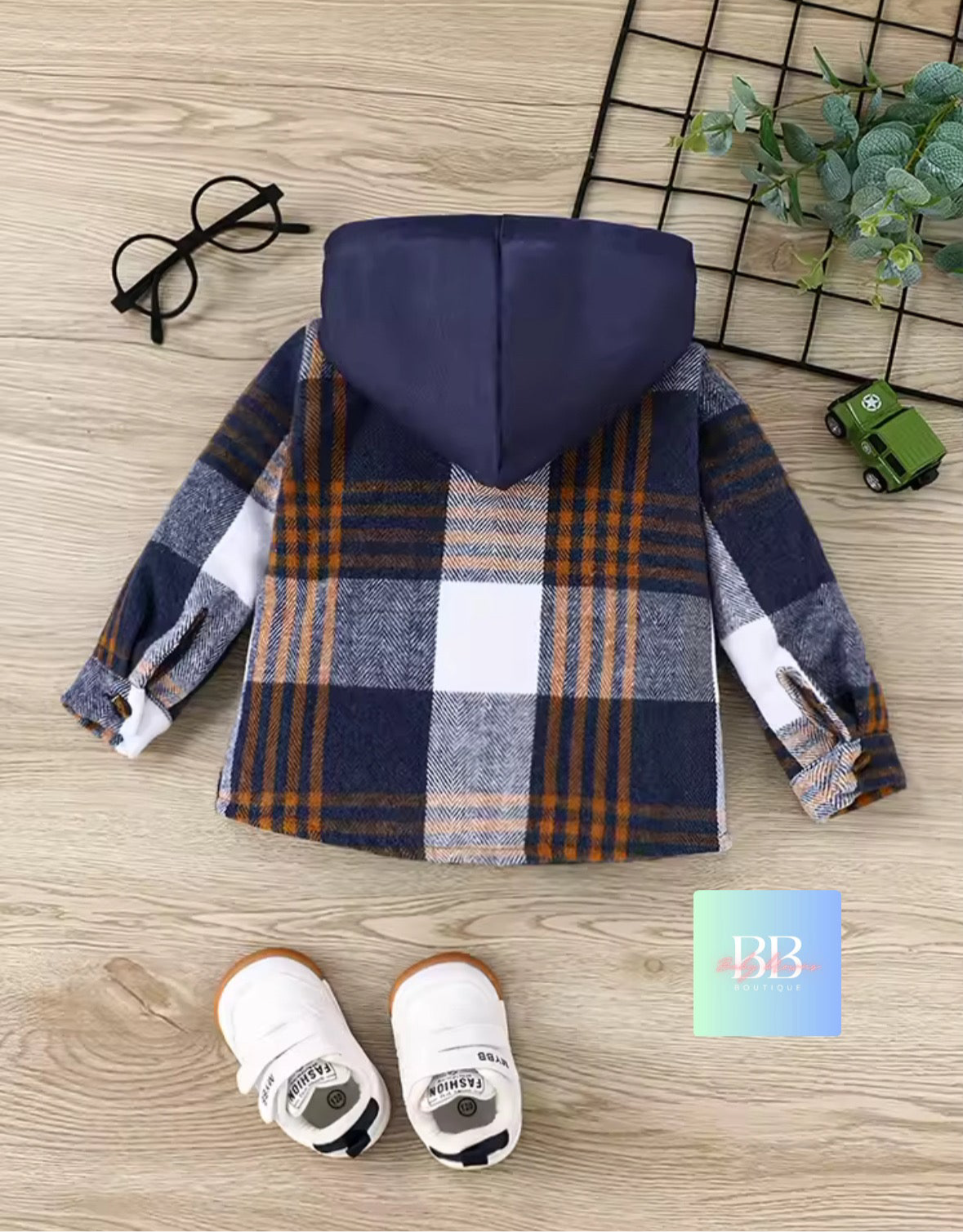 Plaid shirt with hood on a wooden surface, accompanied by baby shoes and a toy car.