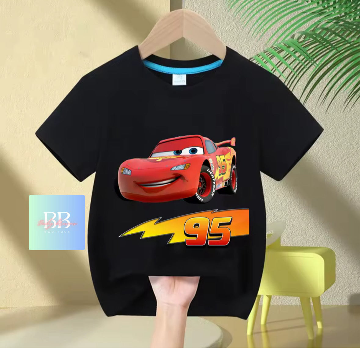 Black t-shirt with a cartoon character and number 95 on a hanger against a light-colored wall.