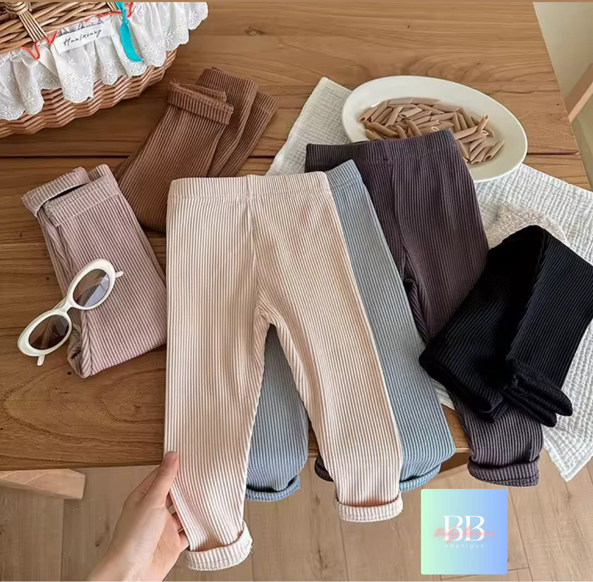 Collection of ribbed tights in various colors on a wooden surface with a hand holding a beige pair.