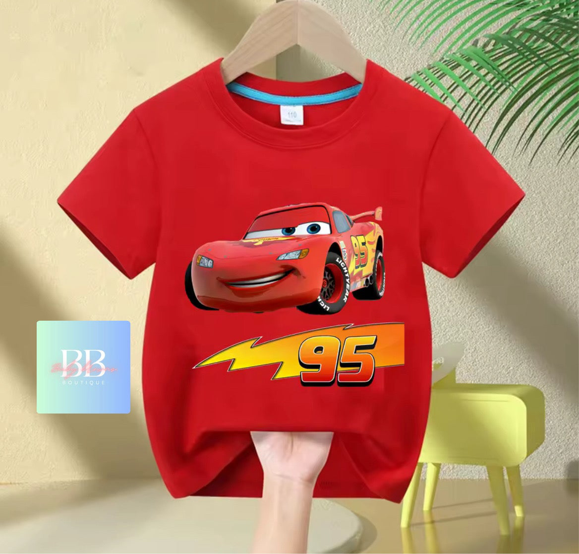 Red t-shirt with a cartoon car design on a hanger against a beige wall.