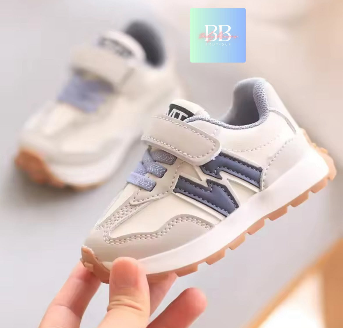 White and gray children's sneakers with a hand holding one shoe on a light background.