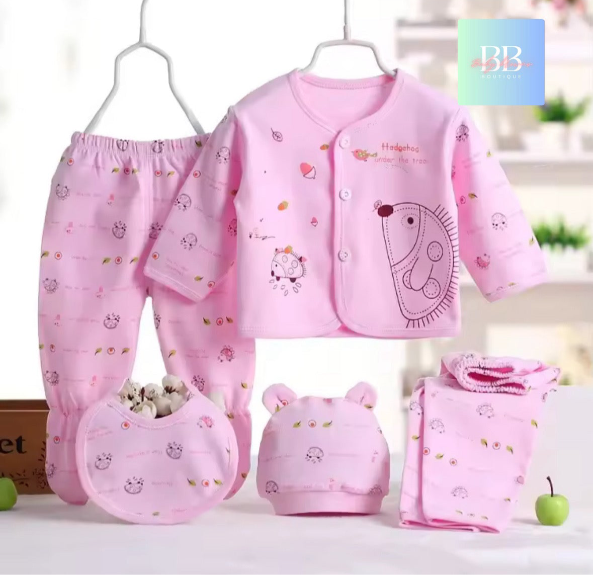 Baby clothing set with pink outfit, pants, hat, and bib on a white background.