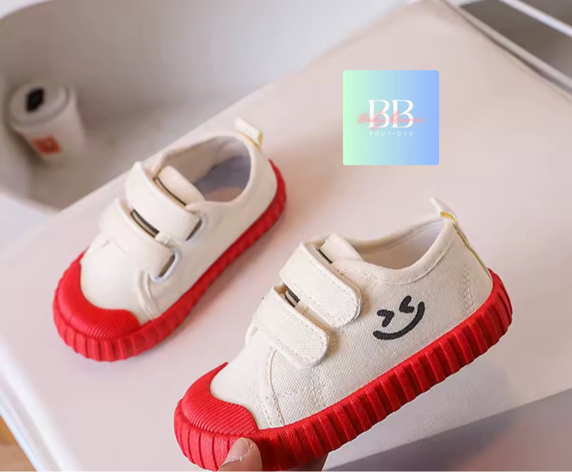 Pair of children's shoes with red soles on a light surface, featuring a visible brand logo.