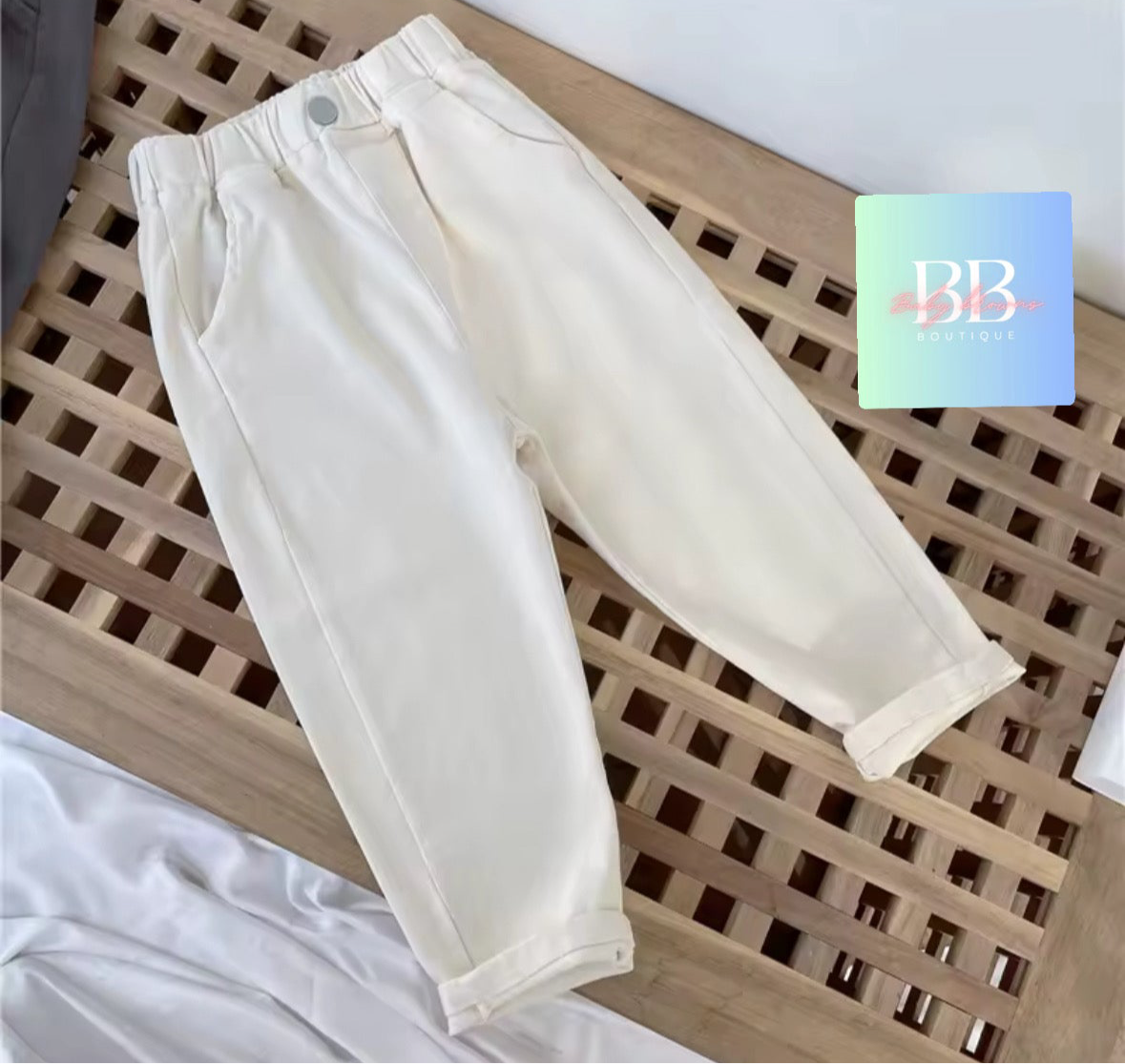 White pants on a wooden surface with a brand logo in the corner.