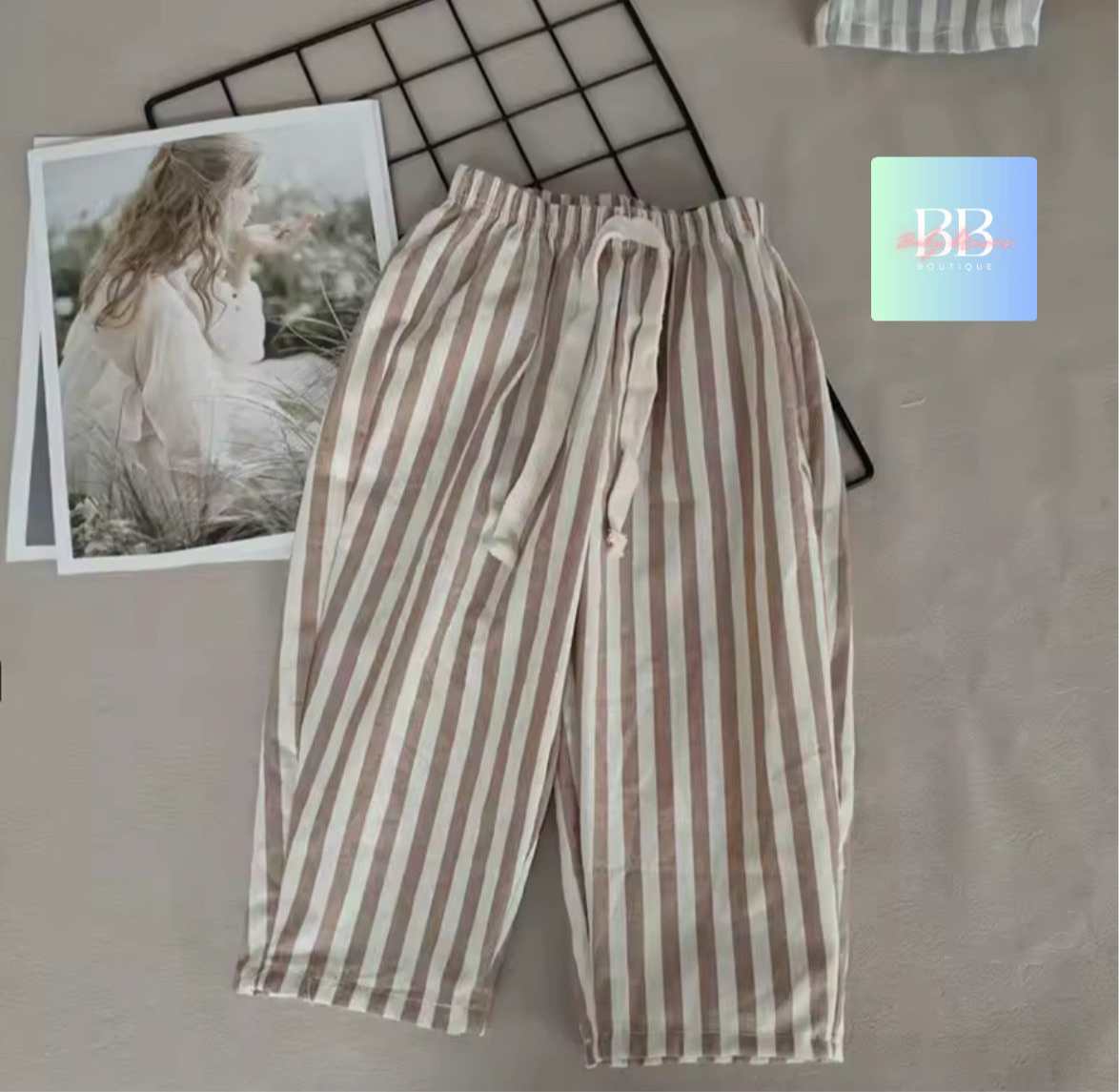 Striped pants on a textured surface with a blurred photo and brand logo in the background