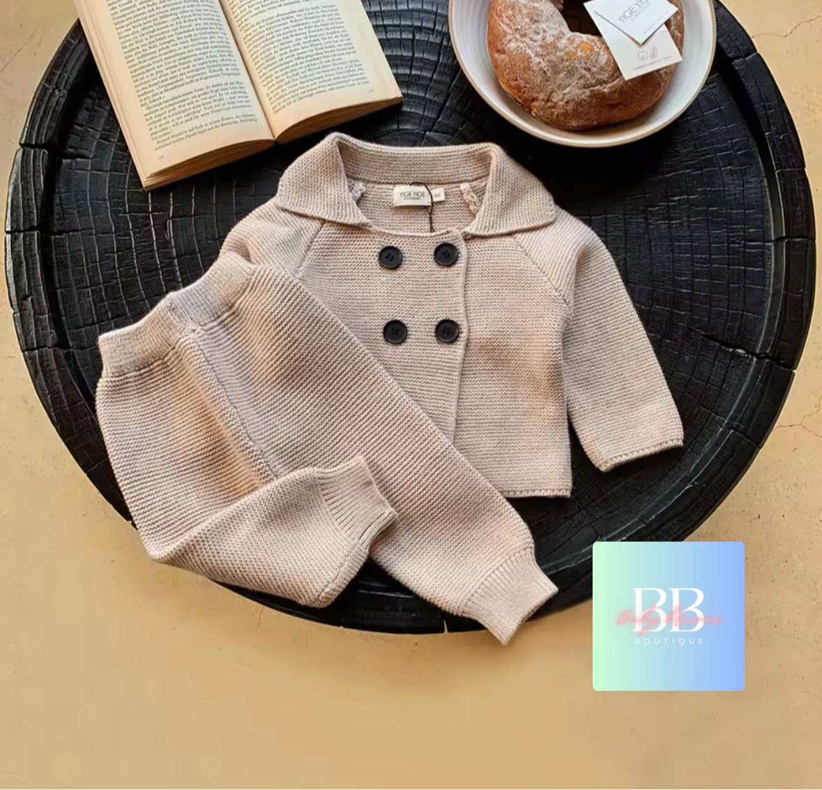 Children's beige coat with black buttons on a dark round surface with a book and pastry.