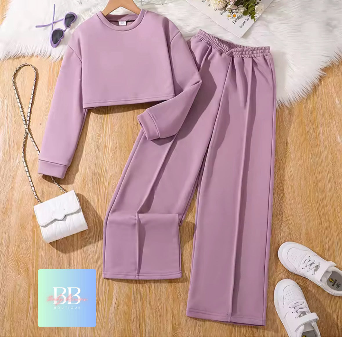 Purple sweatshirt and pants set on a wooden surface with a white bag and sneakers.