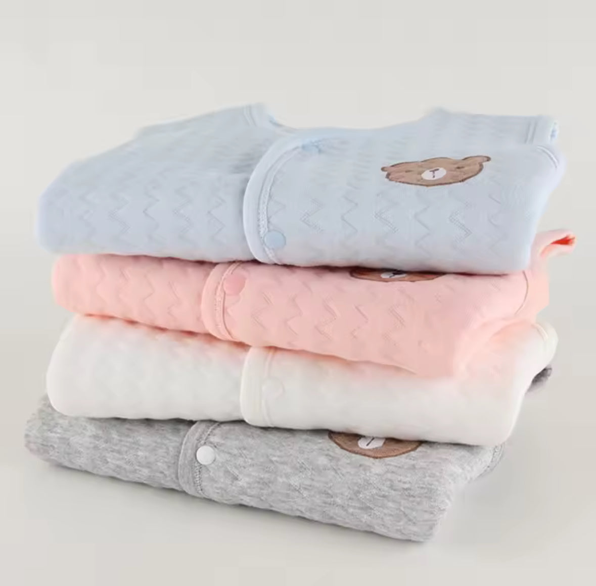 Stack of folded baby clothes with bear designs on a light gray background soft cotton waistcoat/bodywarmer