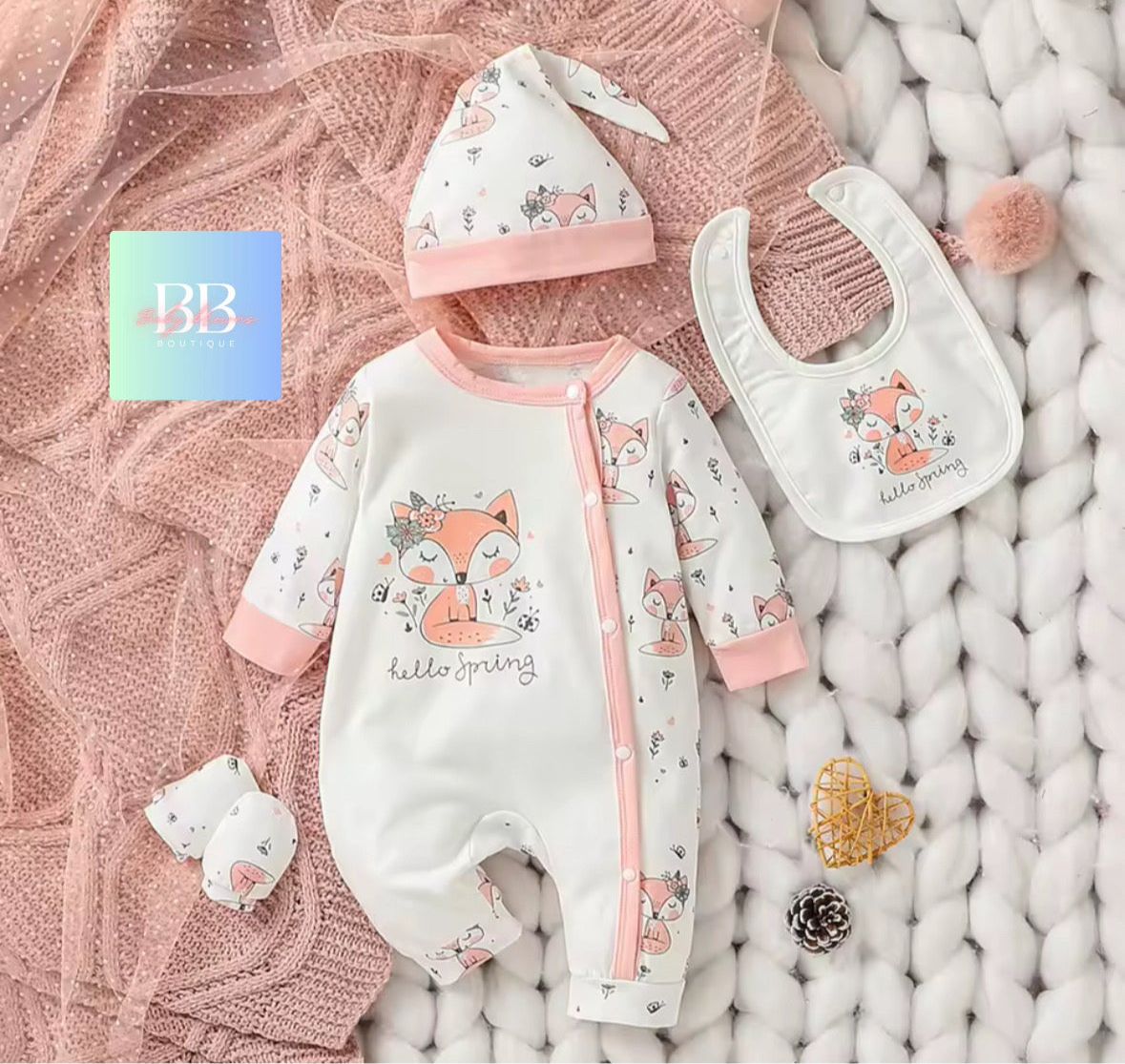 Baby outfit set with onesie, hat, bib, and toy on a textured pink blanket