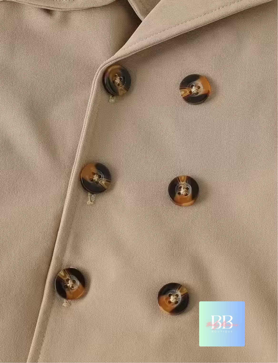 Close-up of a beige coat with tortoiseshell buttons, featuring the brand 'BB'.