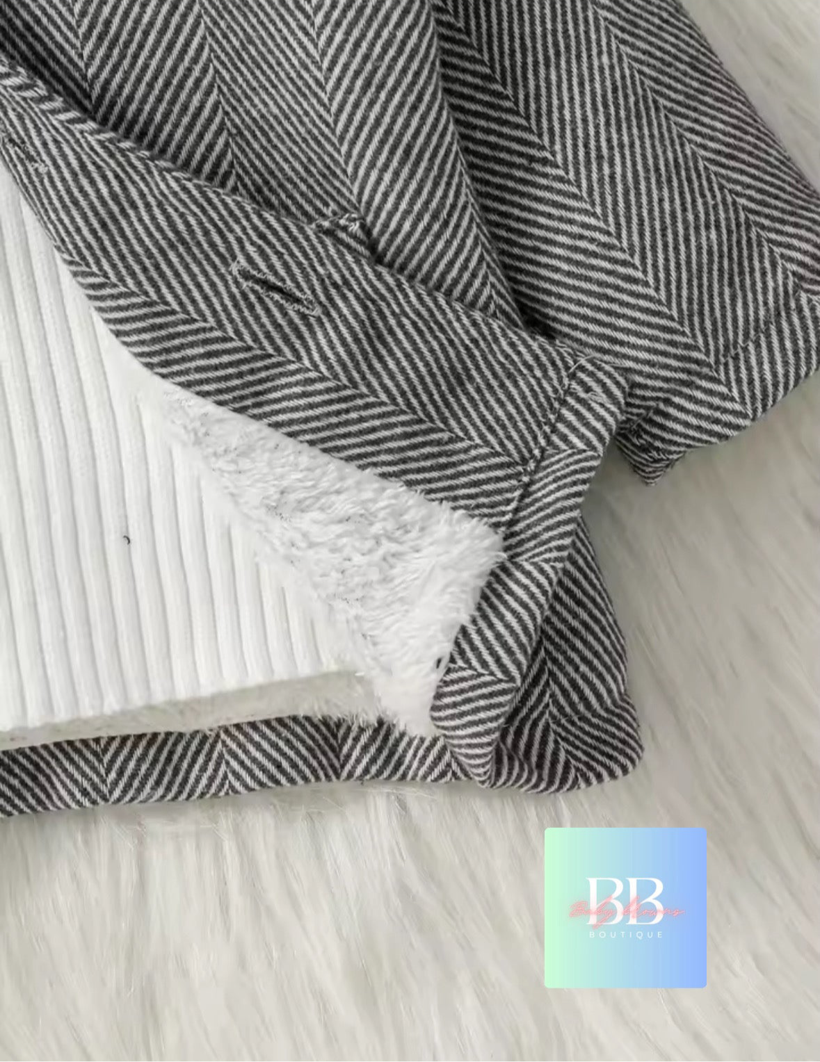 Gray and white herringbone blanket with fluffy white lining on a light wooden surface.