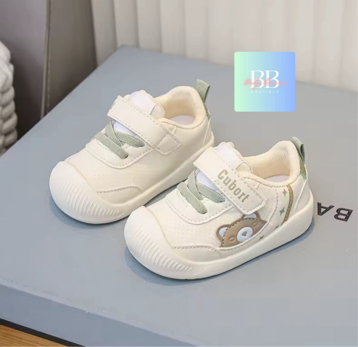 Pair of children's white sneakers with green accents on a light blue surface.