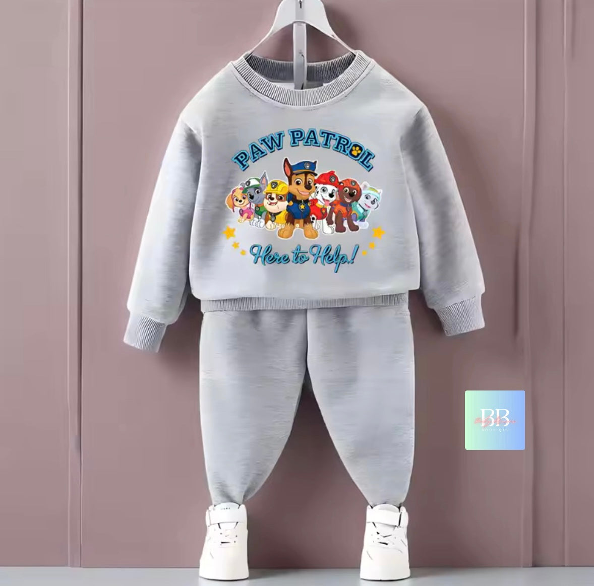 Children's gray sweatshirt and pants set with Paw Patrol design on a hanger against a purple background.