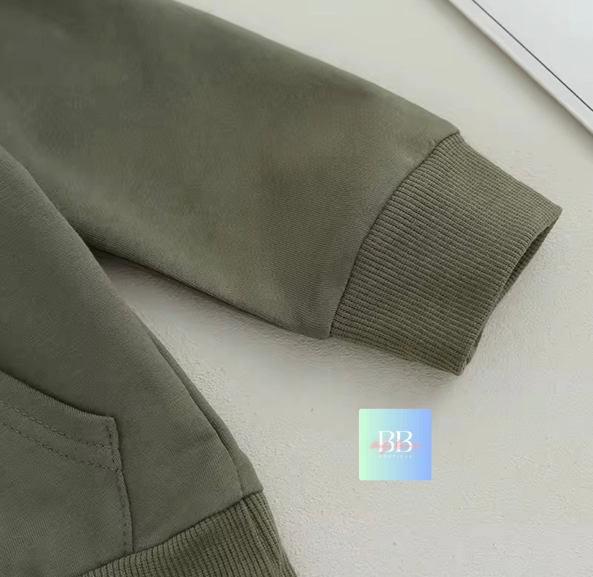 Close-up of a green jacket sleeve on a light gray surface with a brand logo in the corner.