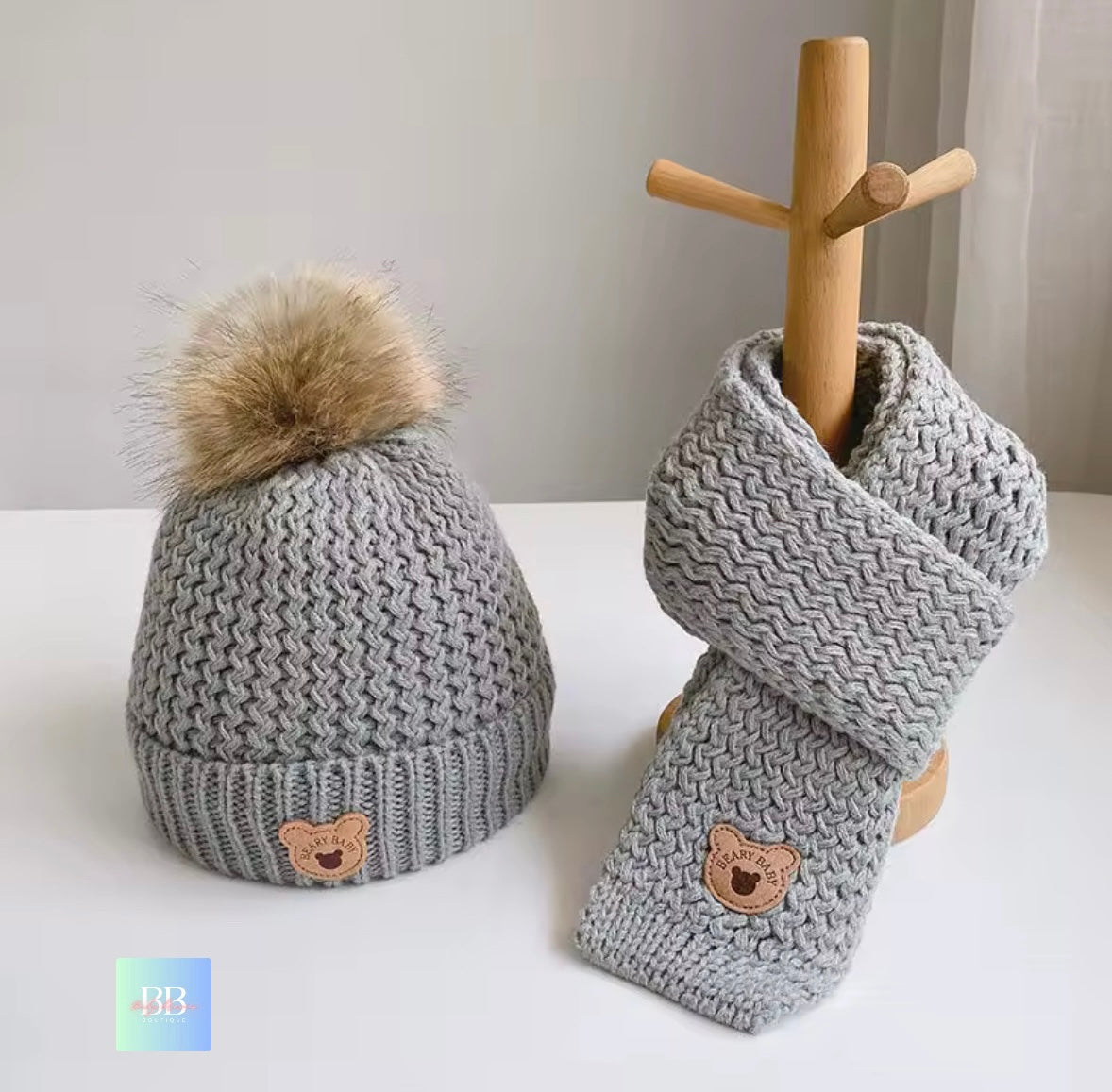 Gray knit hat and scarf set with bear face details on a white surface.