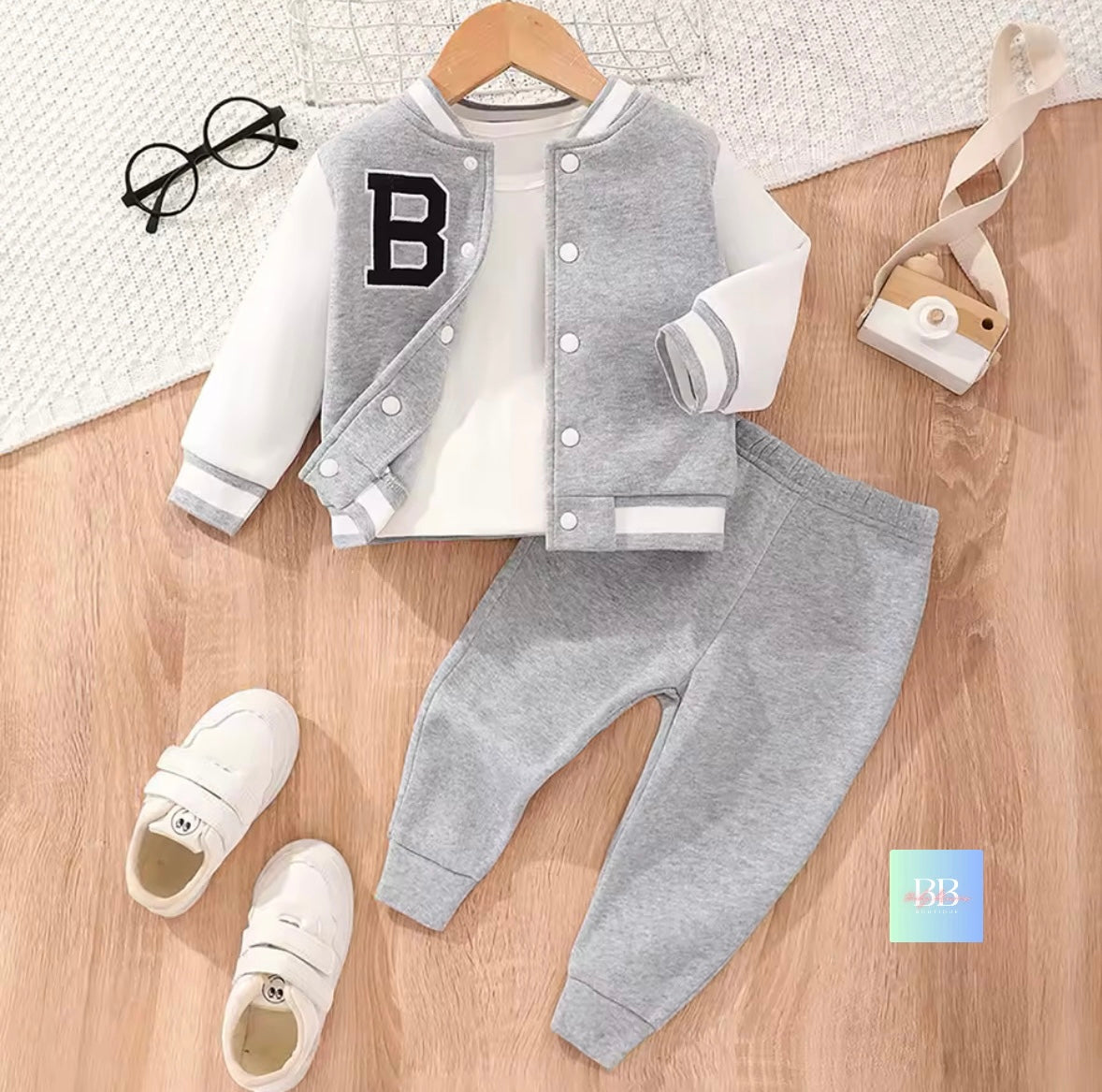 Children's gray varsity jacket with letter 'B', white shirt, gray pants, and white sneakers on a wooden surface.
