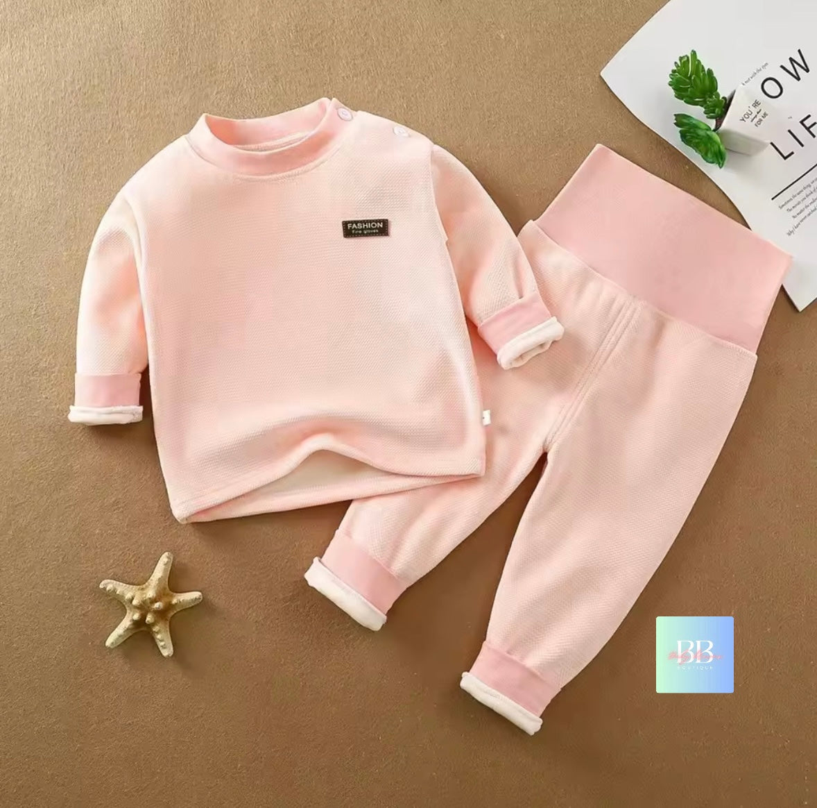 Pink children's outfit with a starfish and magazine on a brown background