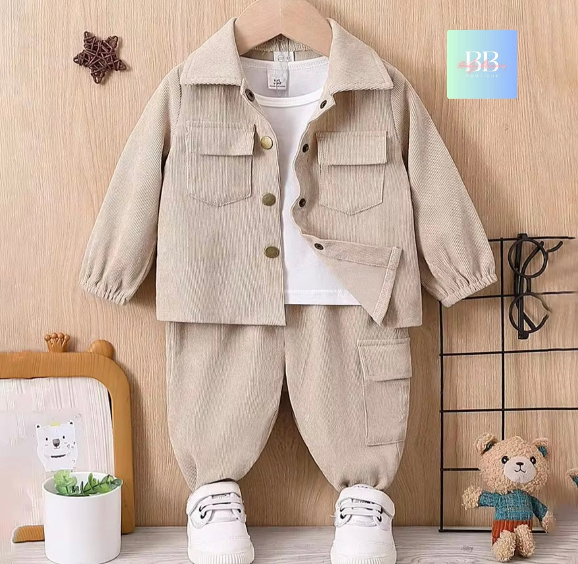 Children's beige jacket and pants set on a hanger against a wooden wall background.