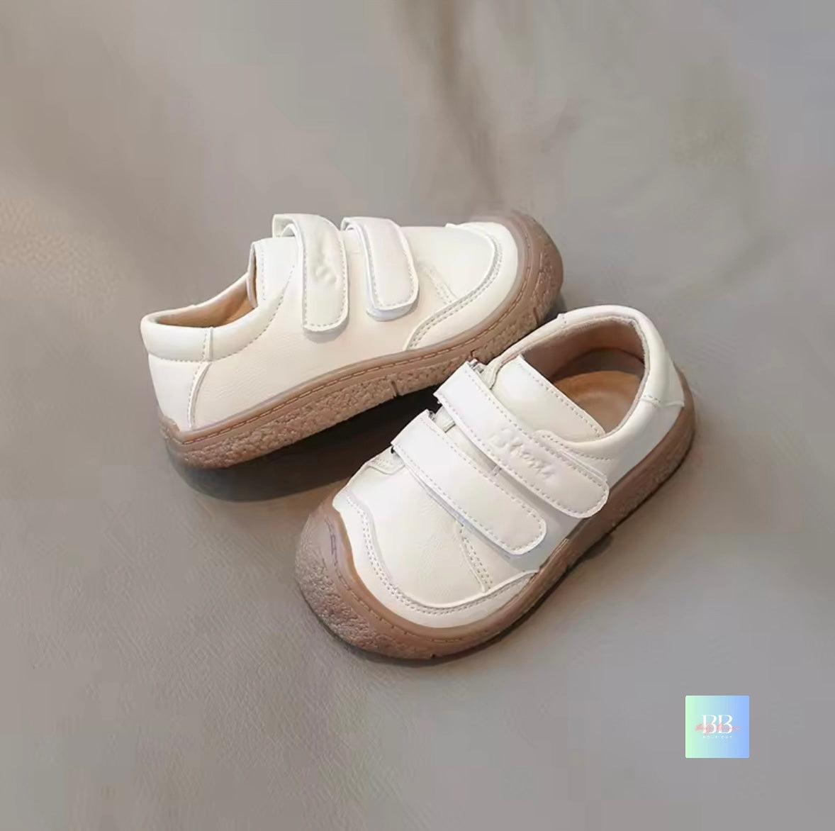 Pair of white children's shoes with brown soles on a gray background