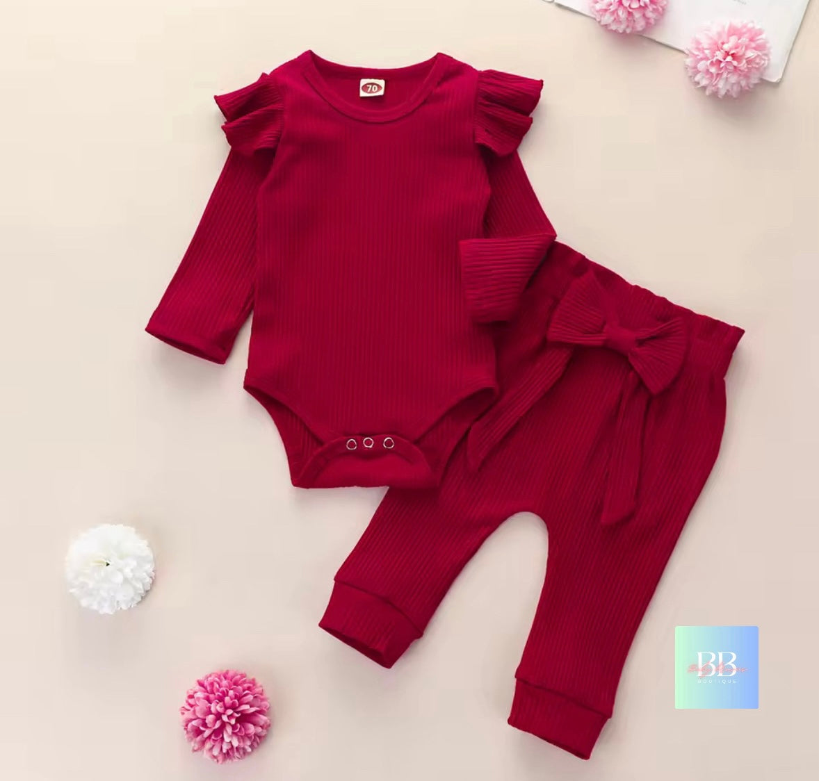 Red baby outfit with ruffled sleeves and bow details on a beige background