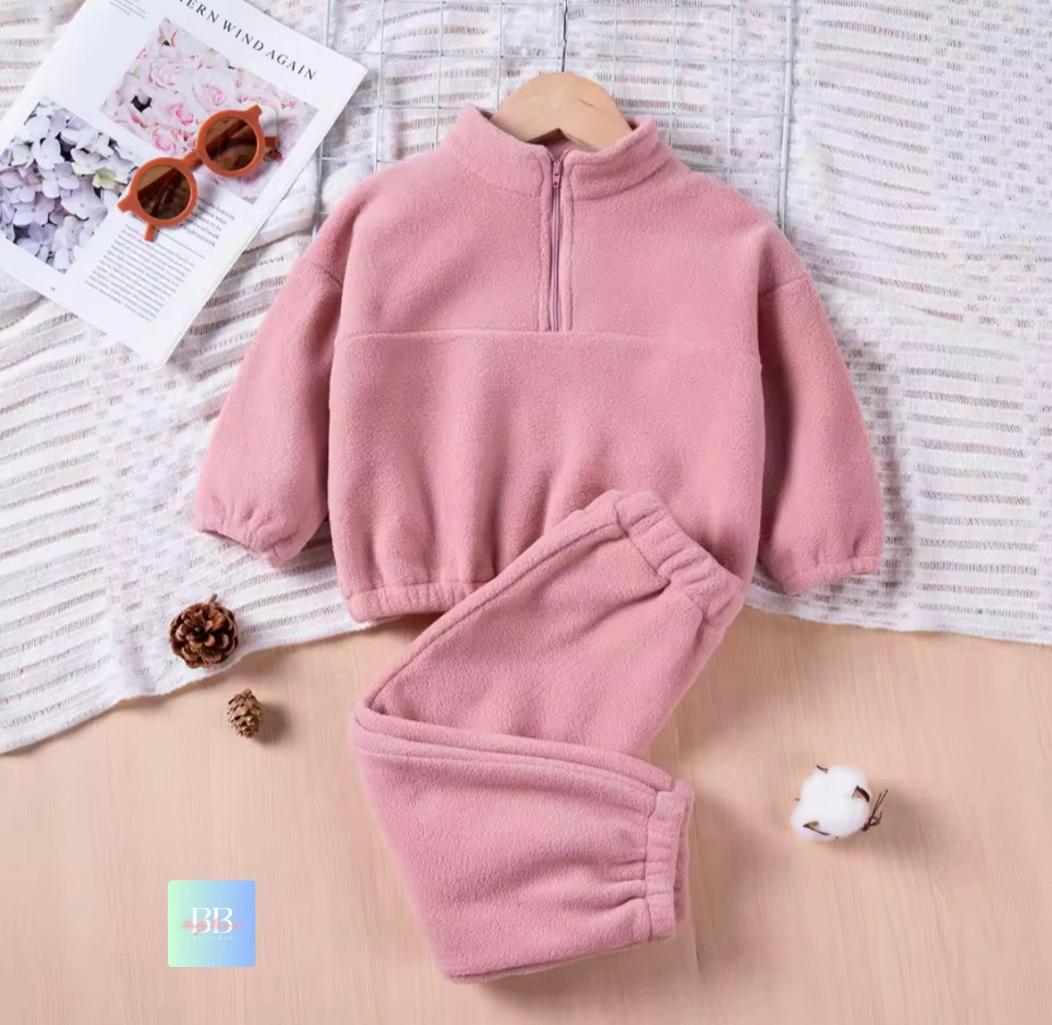 Pink fleece set on a textured surface with a magazine and sunglasses.