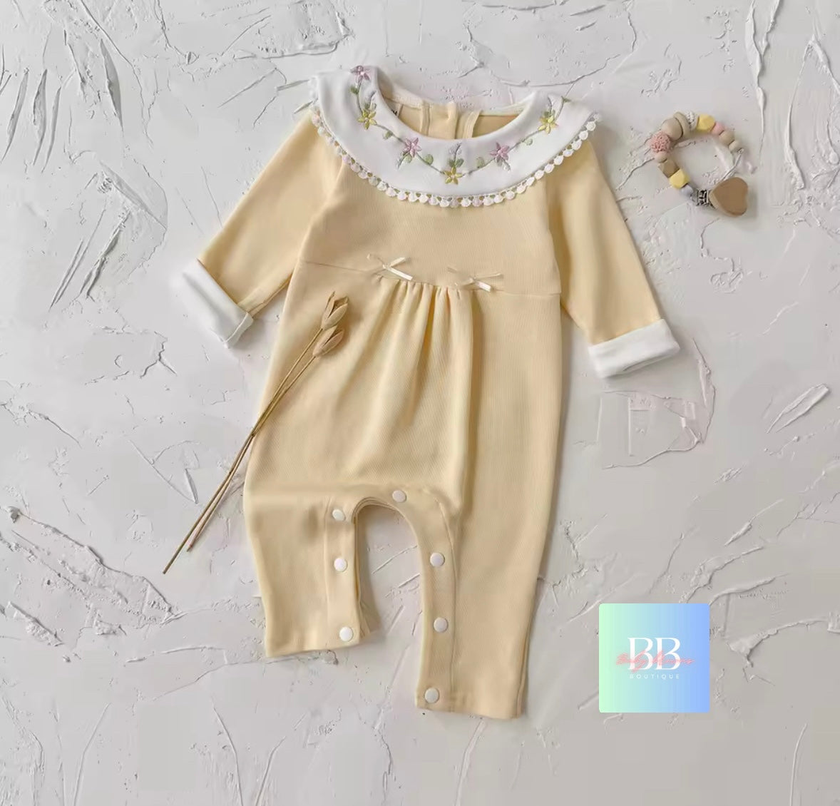 Beige baby romper with floral collar on a textured white background
