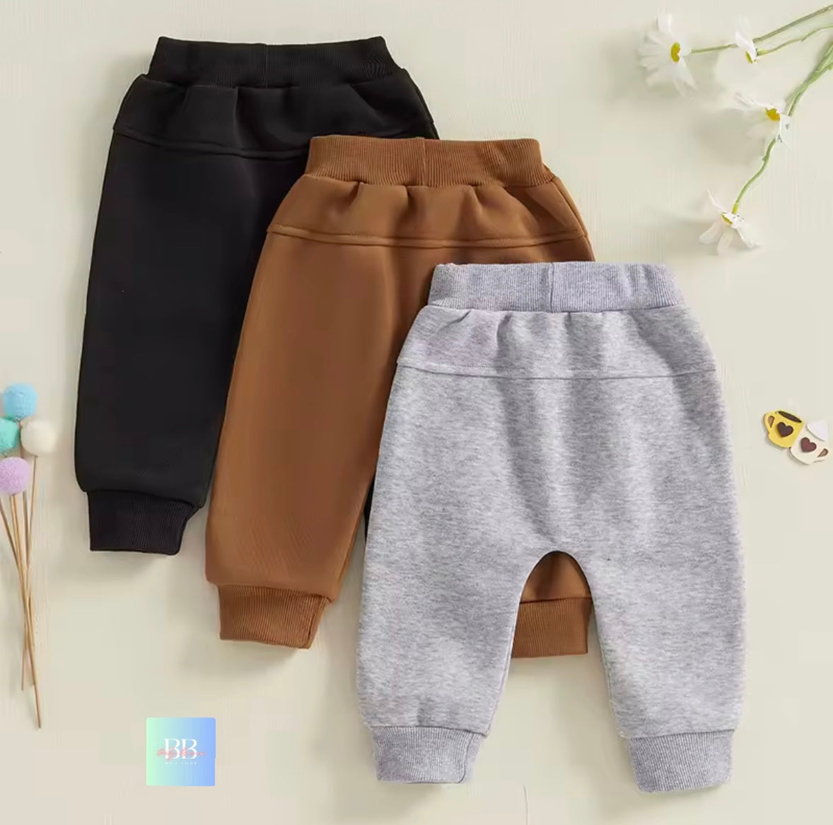 Three pairs of children's pants in black, brown, and gray on a light background.