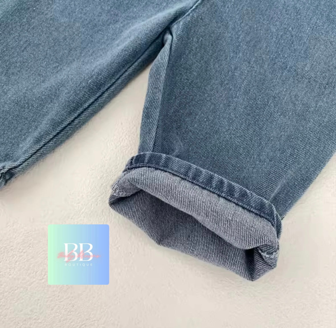 Close-up of blue jeans on a white background with a brand logo in the corner.