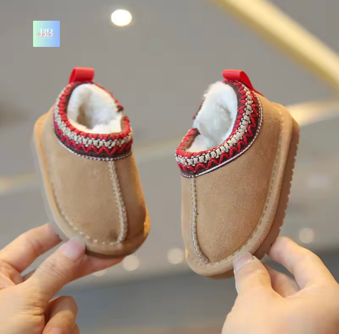 Pair of baby shoes with red and white accents held by a person against a blurred background.