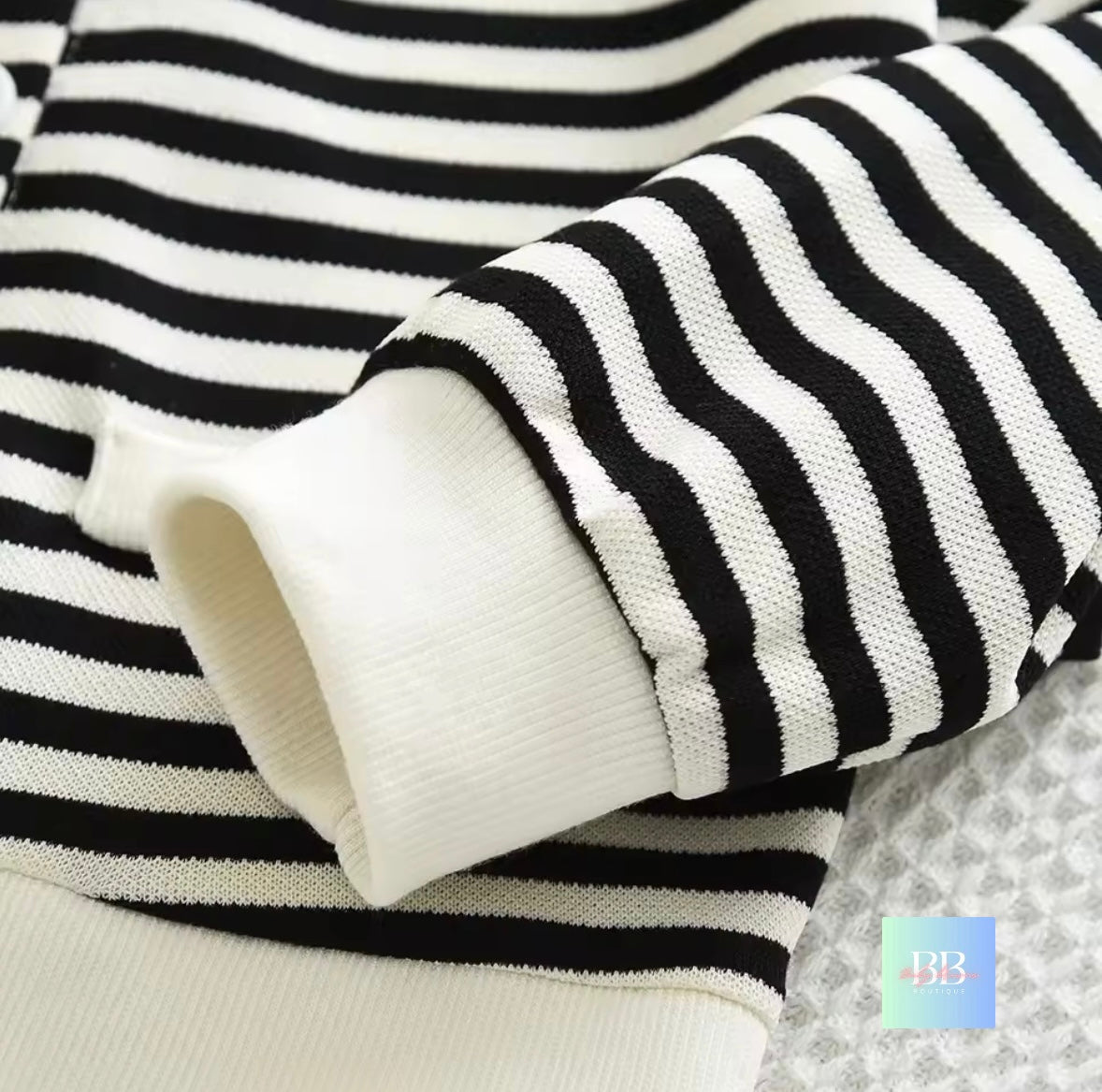 Close-up of a black and white striped sweater with a blurred brand logo in the corner.