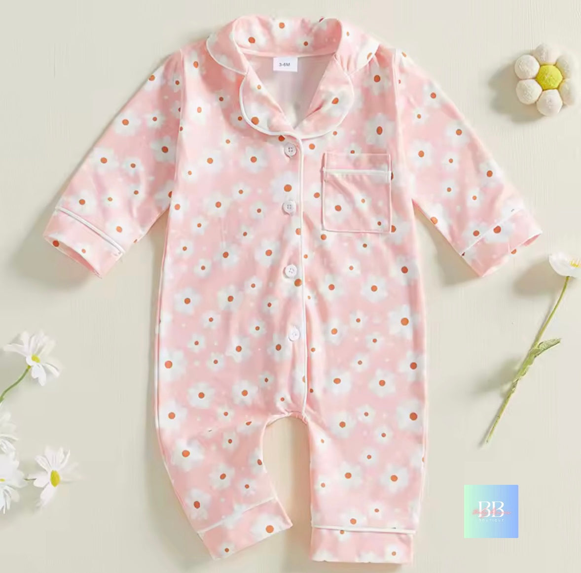 Pink baby onesie with white daisy pattern on a light beige background