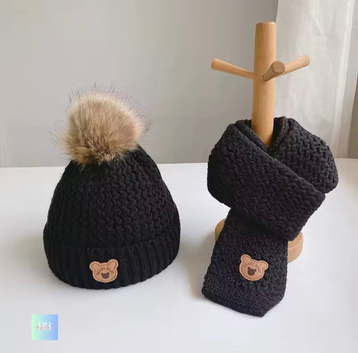 Black knit hat and scarf set with bear emblem on a white surface