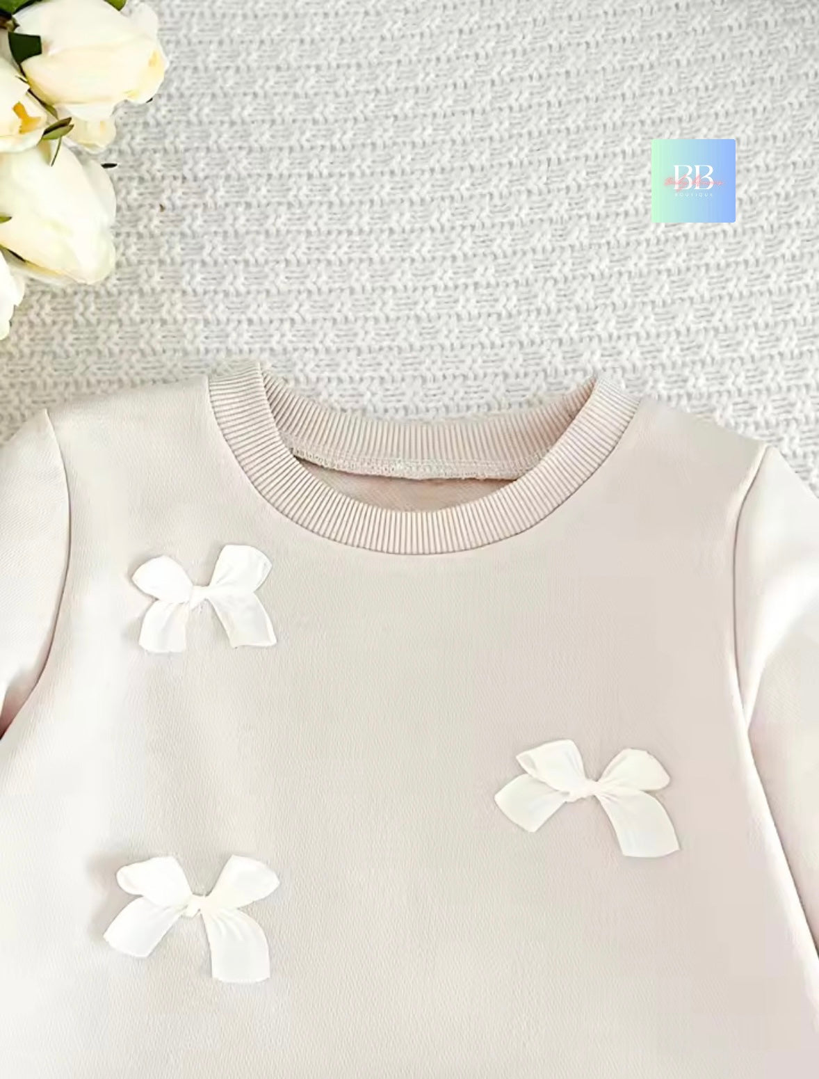 Light pink sweater with white bow details on a textured gray background