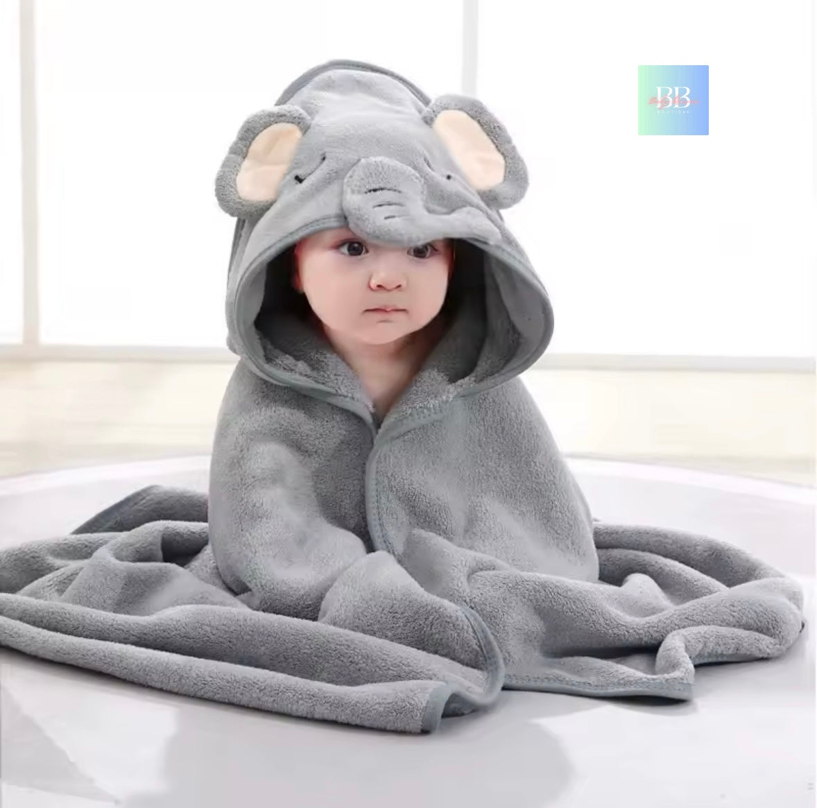 Child wearing a gray elephant hooded towel on a white surface