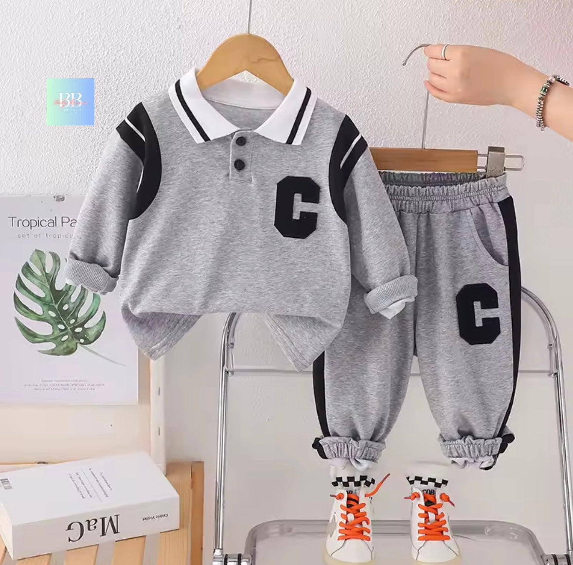 Children's gray outfit with letter 'C' design on a hanger against a light background.
