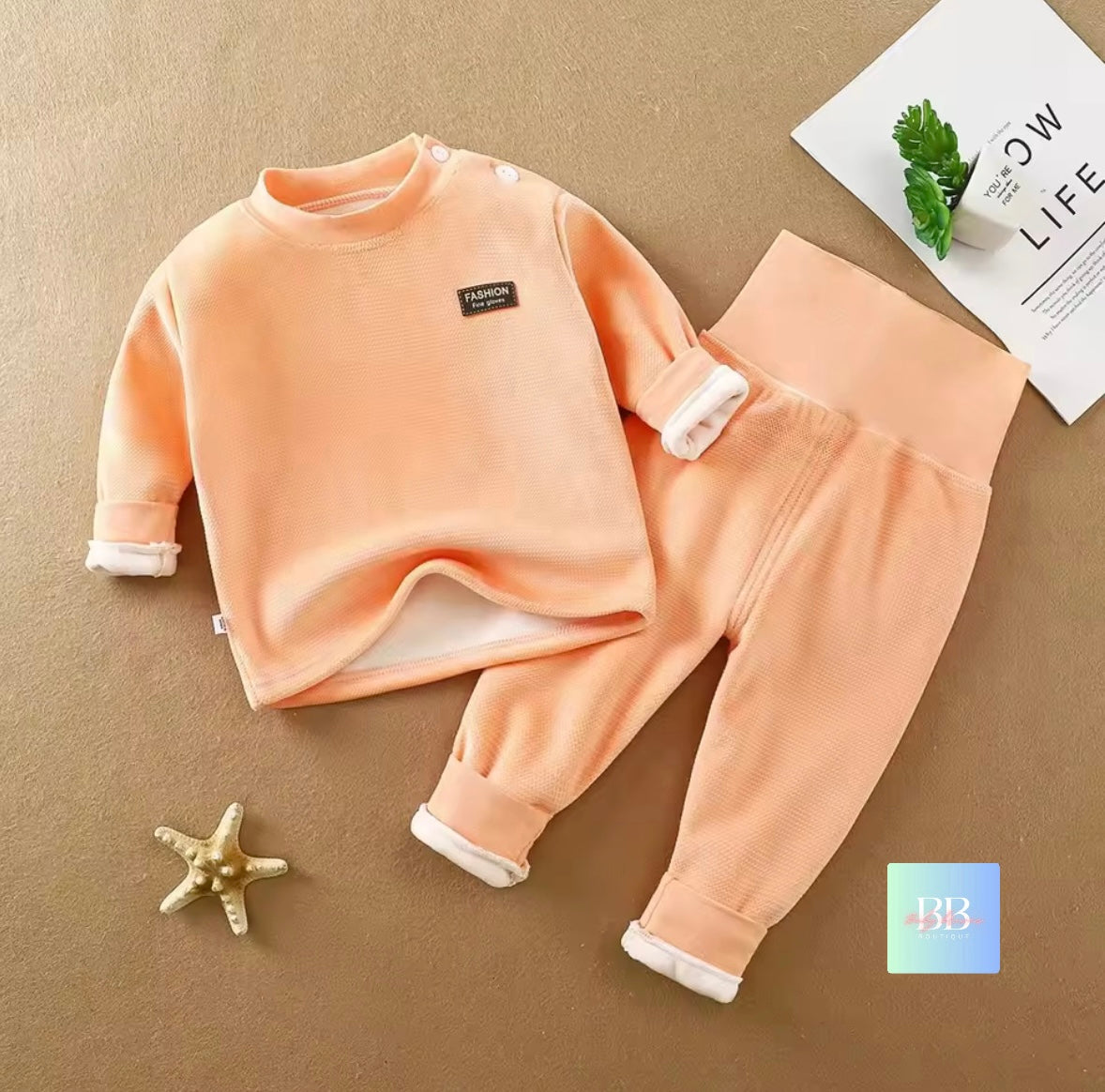 Children's peach-colored outfit with white trim on a beige surface.