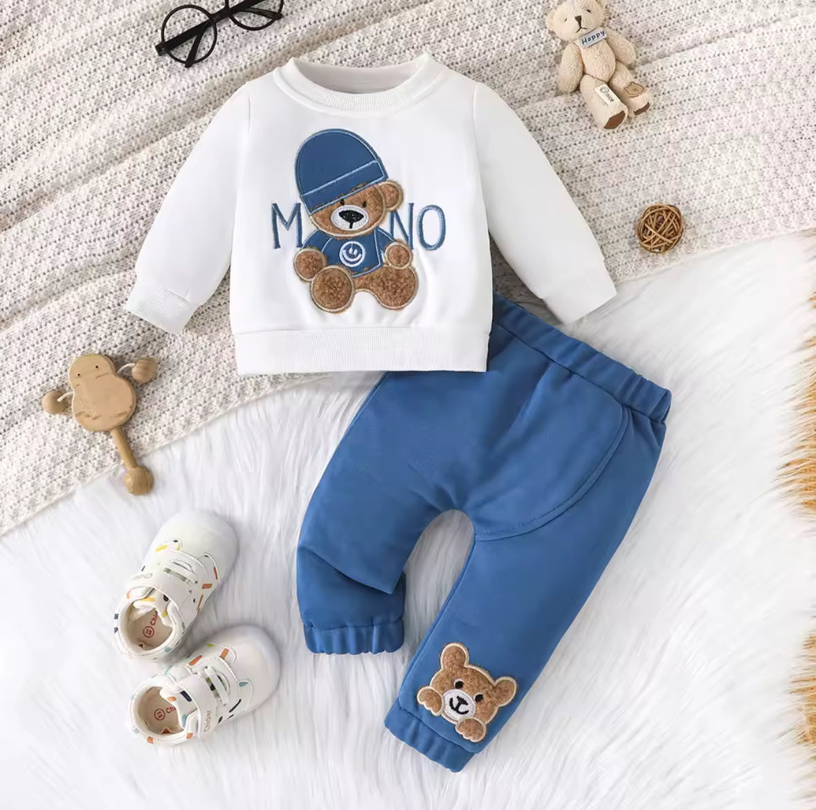Children's outfit with white shirt and blue pants featuring teddy bear designs on a textured surface.