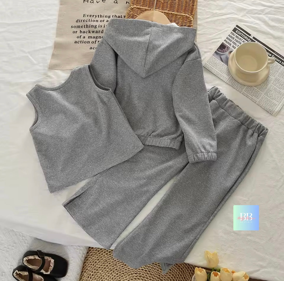 Gray hoodie set on a white surface with a newspaper and cup in the background