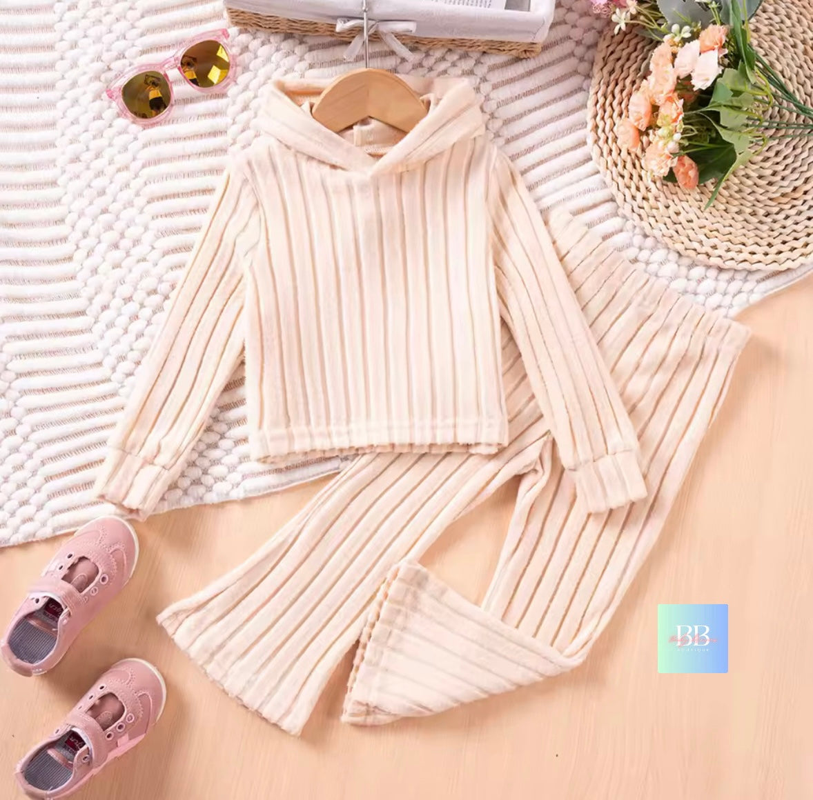 Knitted outfit with a sweater and skirt on a textured surface, accompanied by pink shoes and a basket.